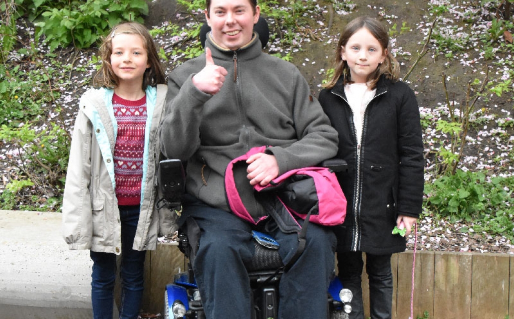 un papa en situation de handicap entouré de ses deux petites filles